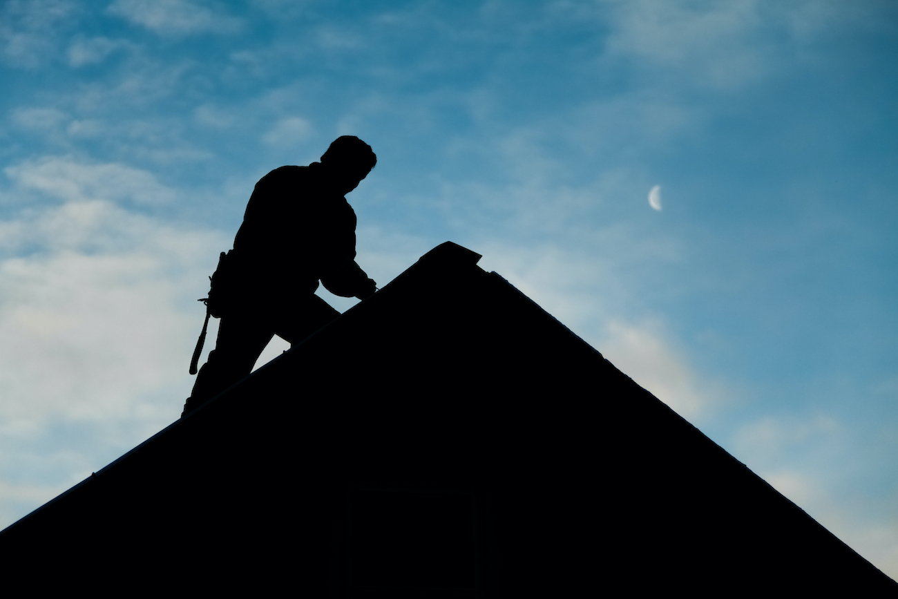Silhouette of roofing contractor finishing Tomball roof repair in the evening
