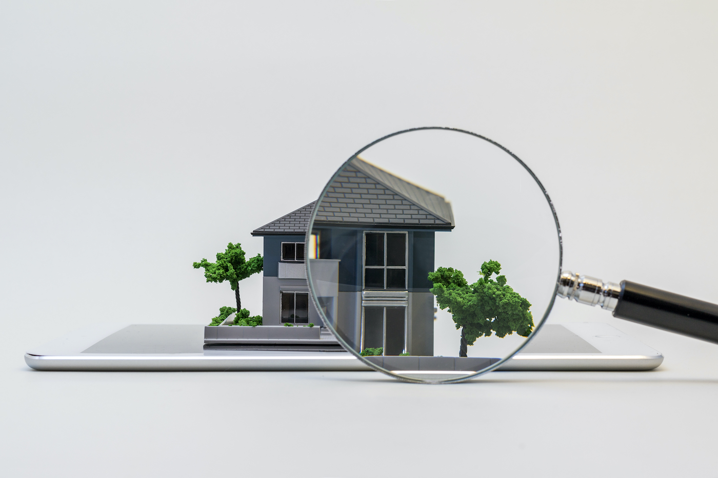magnifying glass held up to the roof on a miniature home model to inspect it