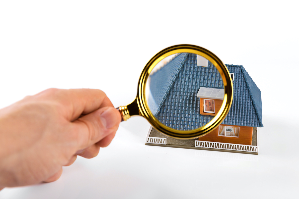 magnifying glass held up to mini home model to symbolize cypress roof inspection