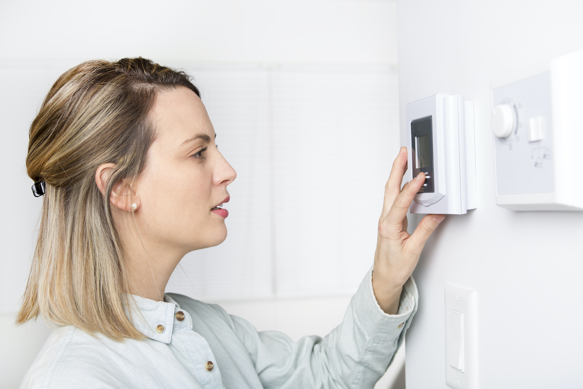 Woman adjusting thermostat in the winter because Sugar Land roof damage has let cold air in