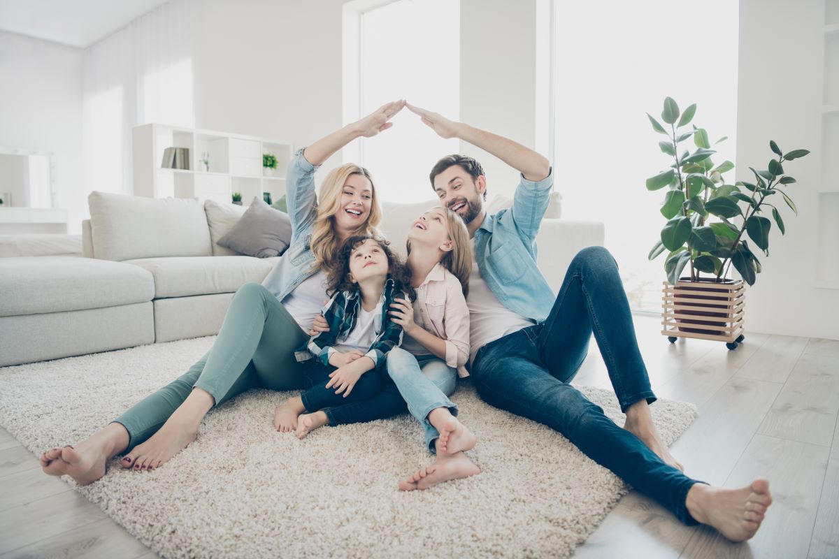 Smiling family sits in living room while parents raise arms to look like Houston roofing
